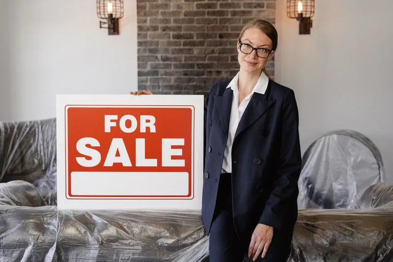 A real estate agent holding a For Sale sign