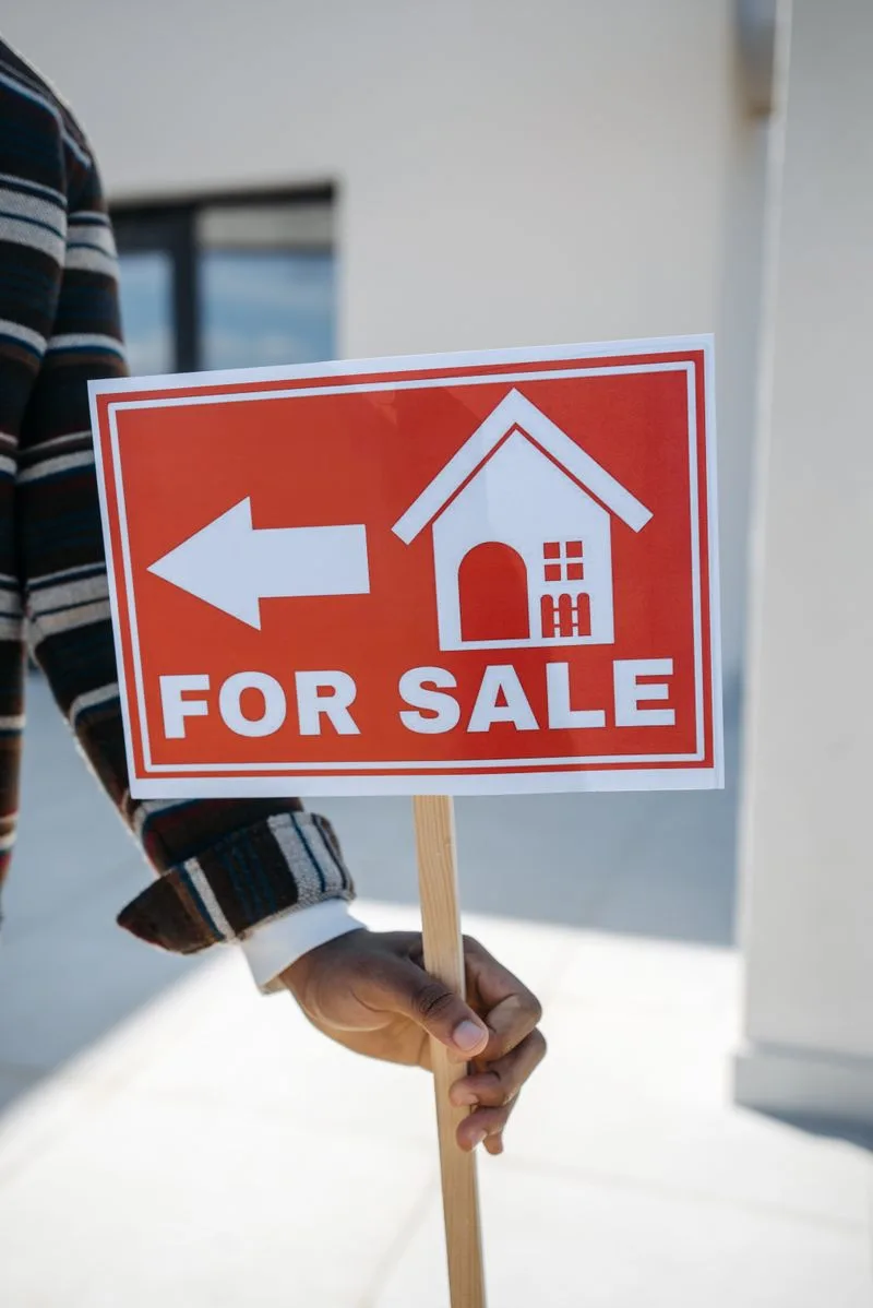 A hand holding a For Sale sign